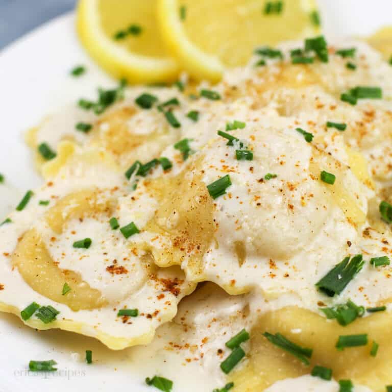 prepared lobster ravioli with cream sauce on white plate with lemon slices on the side