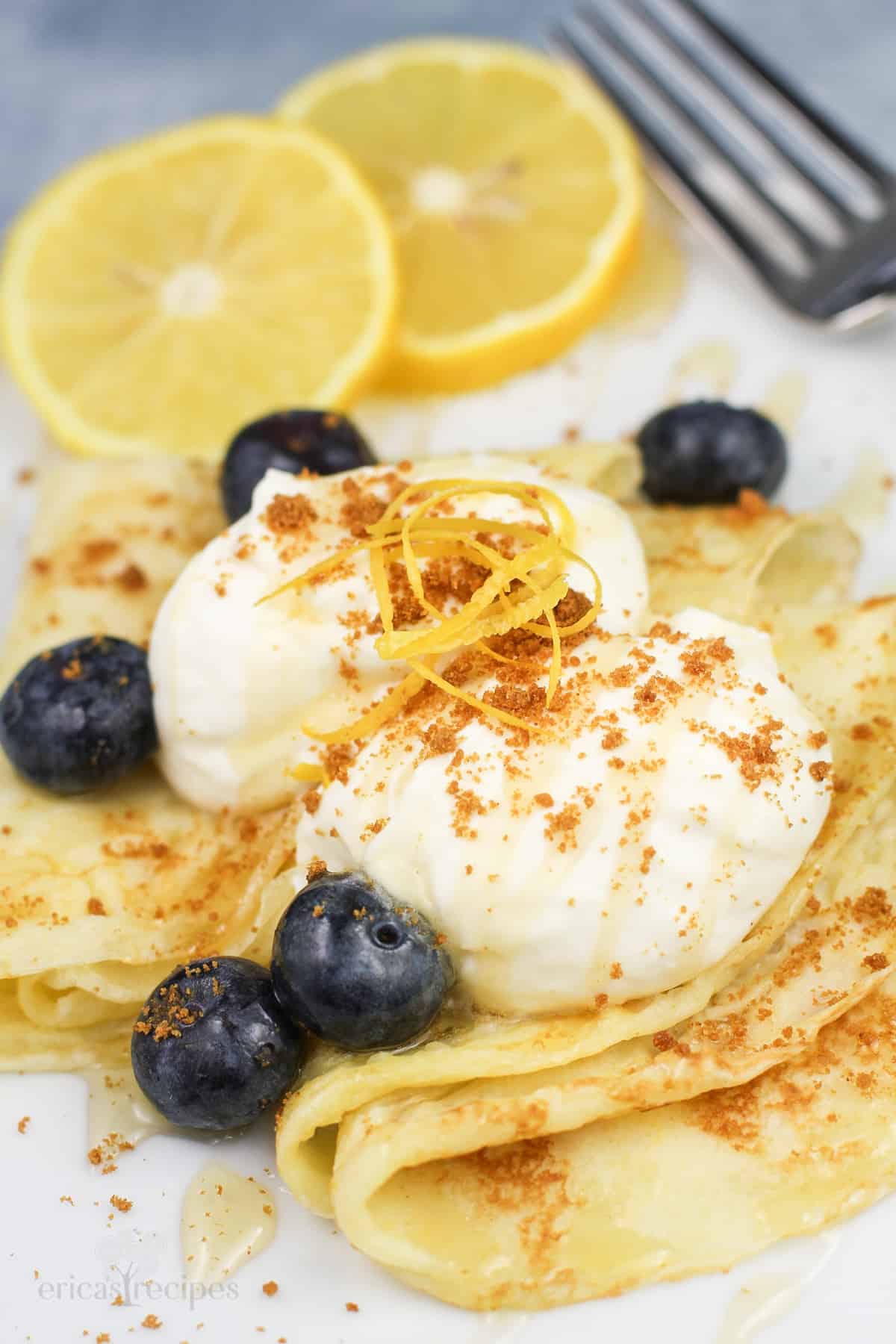 lemon mascarpone and blueberries on top of folded lemon crepes on white plate