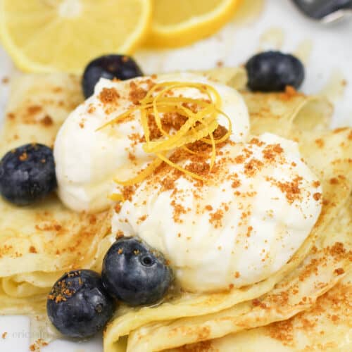 lemon mascarpone and blueberries on top of folded lemon crepes on white plate