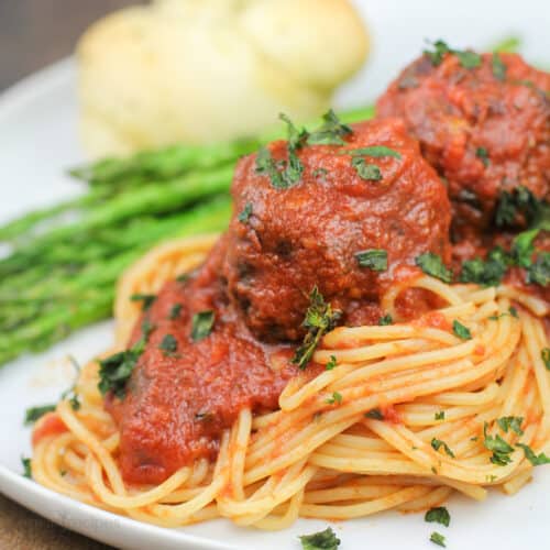 plated portion of smoked meatballs marinara on sauce on spaghetti (asparagus and roll in background)