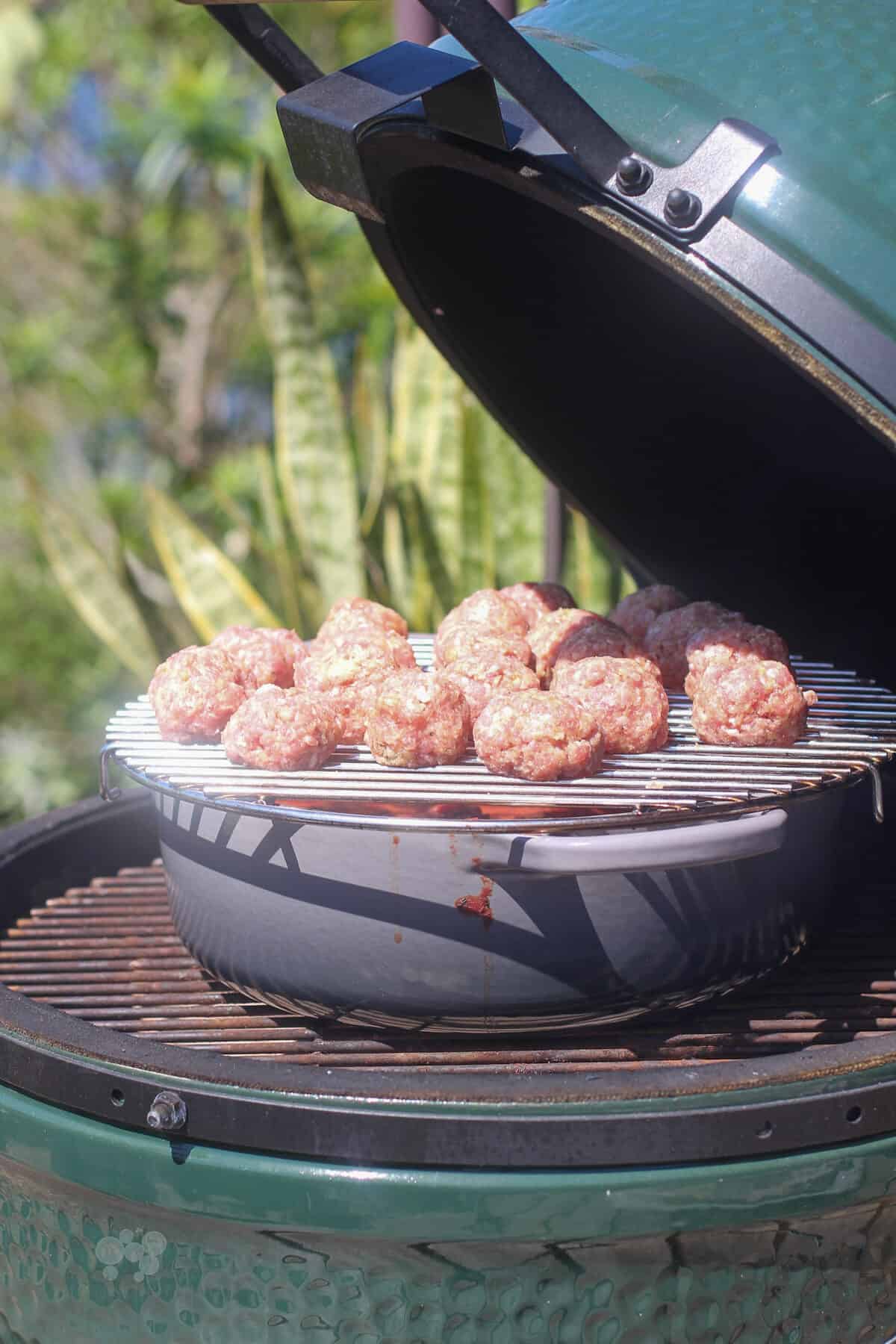 uncooked meatballs on rack on dutch oven in big green egg (side view)