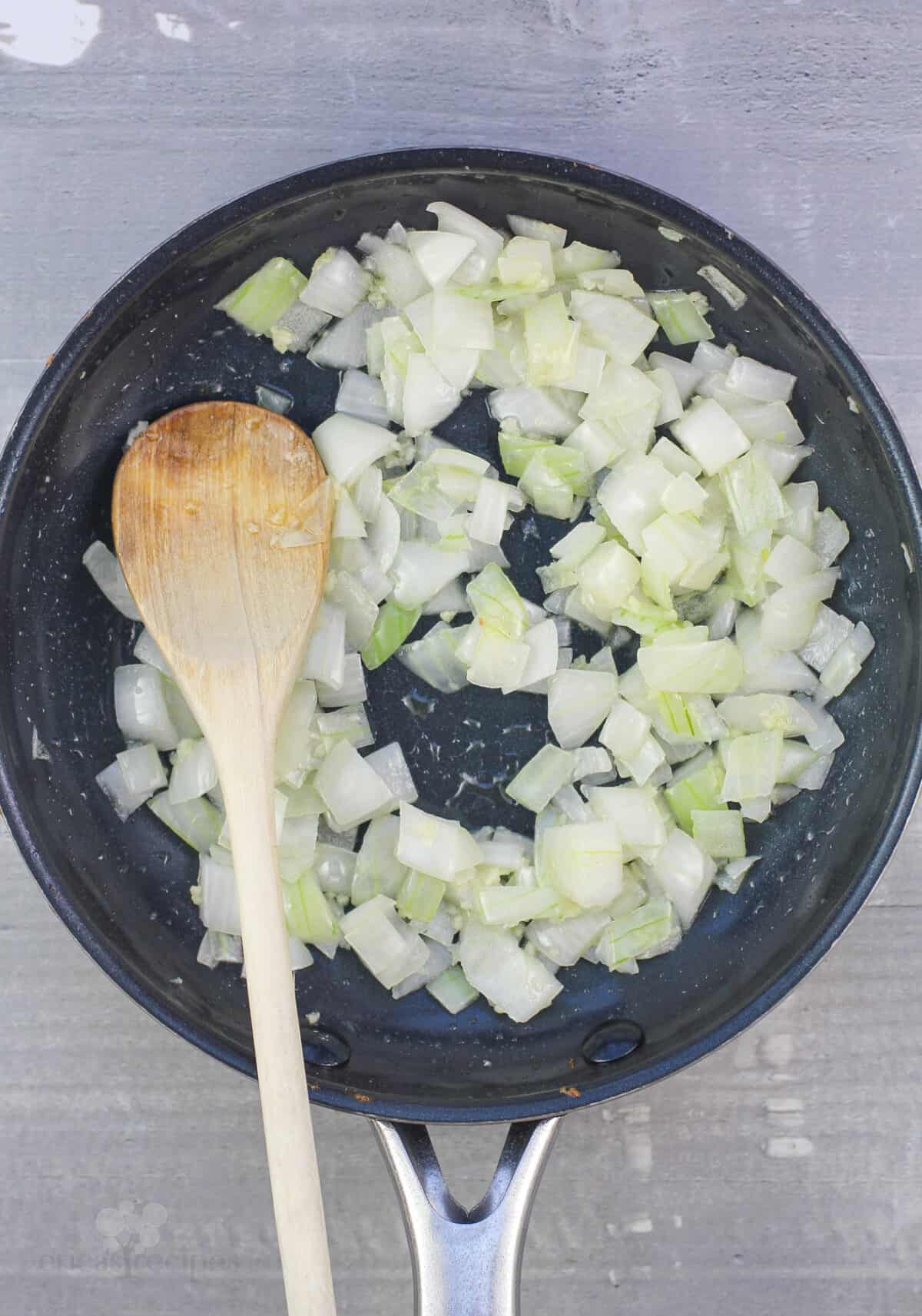 onion, garlic, and wood spoon in skillet