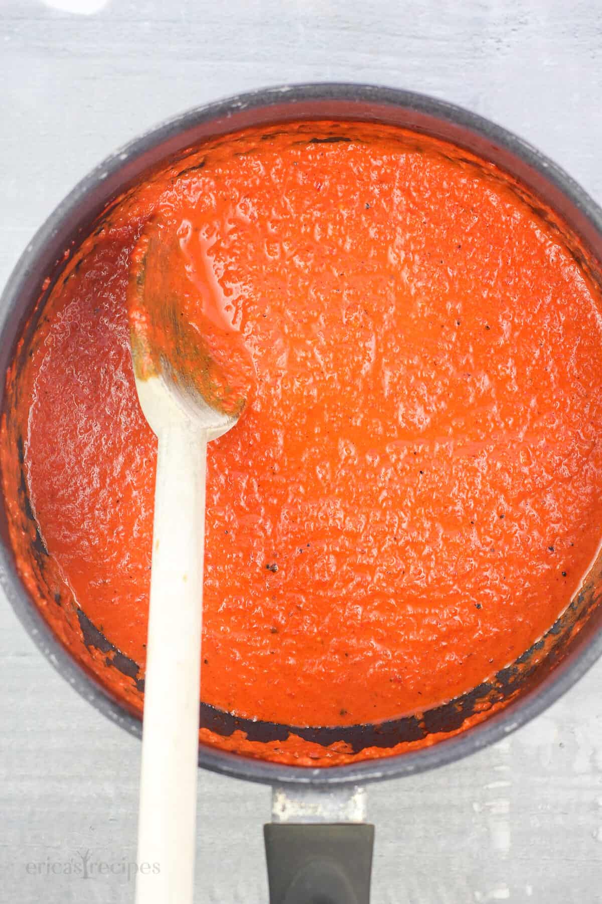 red pepper sauce in saucepan with wood spoon