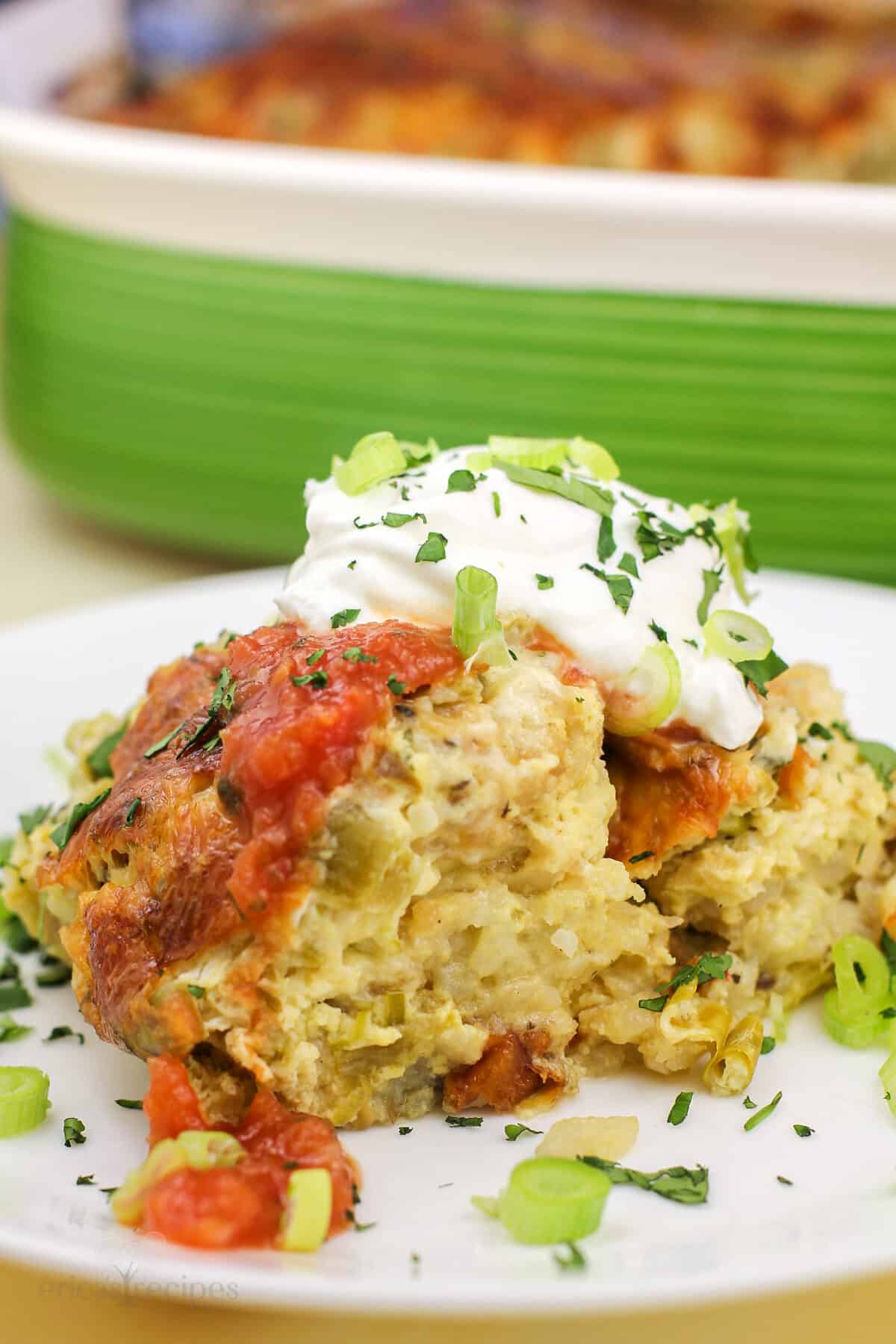 green chile egg bake on white plate topped with garnish; green casserole dish in background