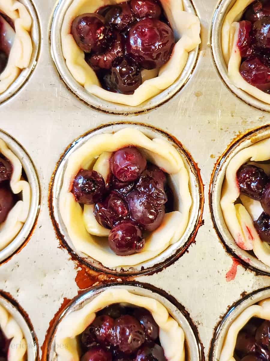 muffin tin with prepared pie crust and filling before baking