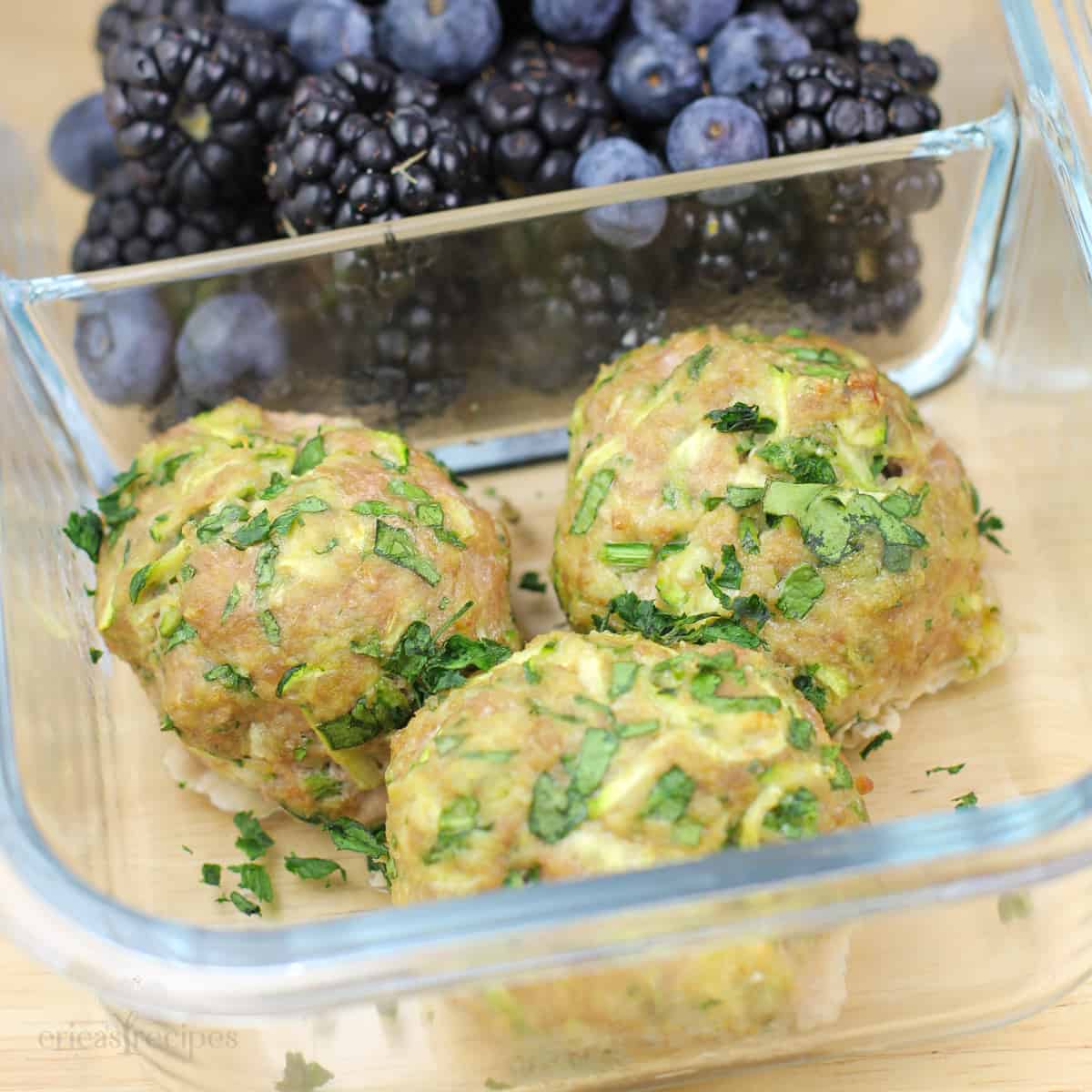 glass container with 3 cooked meatballs in 1 compartment, blackberries in the other compartment