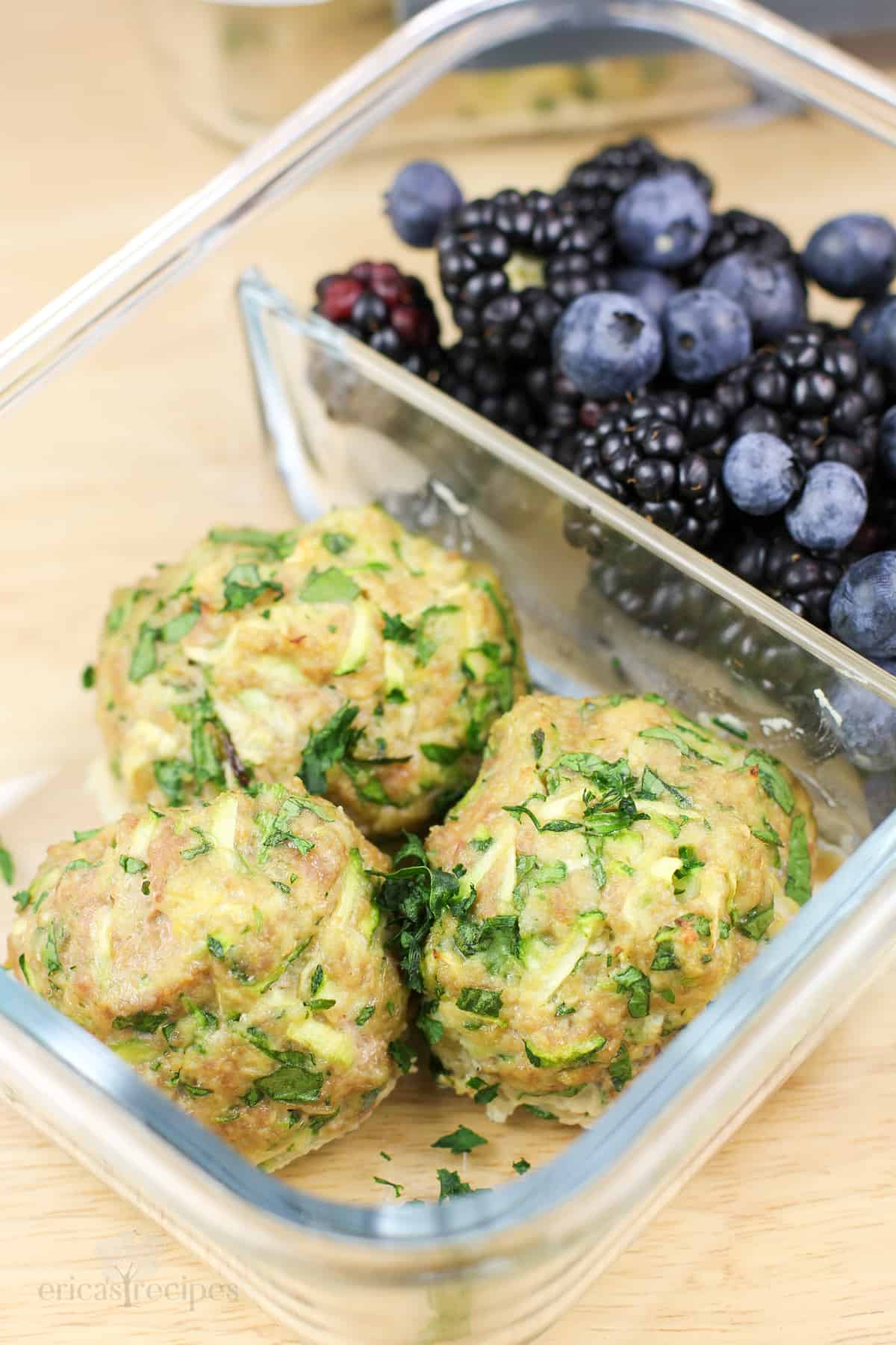 glass container with 3 cooked meatballs in 1 compartment, blackberries in the other compartment