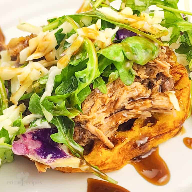 prepared whiskey pulled pork and waffles topped with apple arugula slaw on white plate