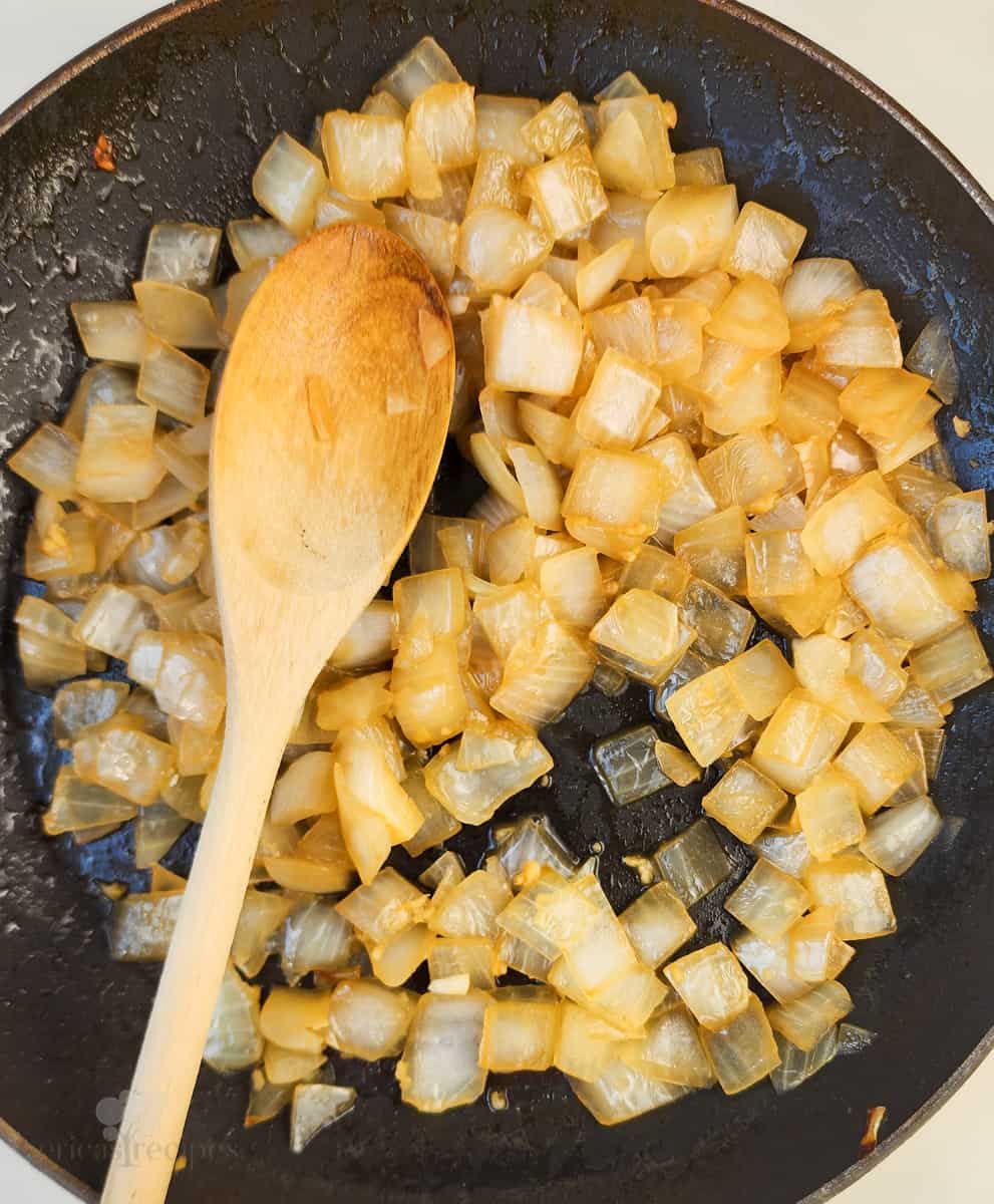 cooked onions in skillet with wood spoon