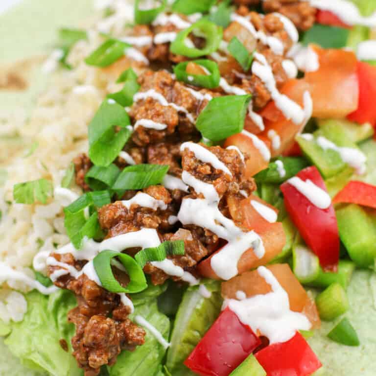 ground beef taco meat atop veggies and rice topped with ranch dressing