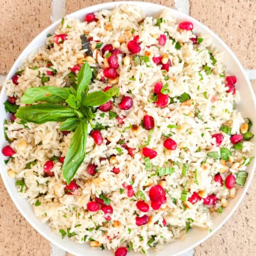 Fresh pomegranate vegan rice pilaf garnished with basil leaves, served in a white bowl on a rustic background